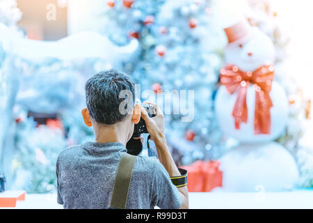 Photographer man take photo of decorated Christmas tree and a snowman. Stock Photo