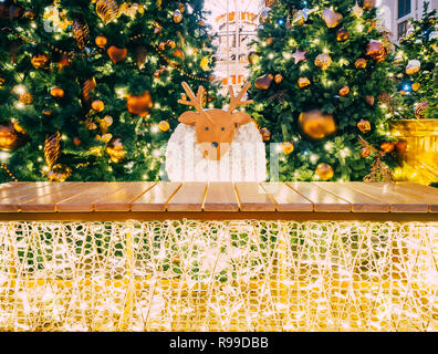 Christmas decorated fir trees with toys and garlands. New Year and Christmas background. Decorative sheep on the background of decorated Christmas trees with light. Wood plank. Postcard layout. Stock Photo