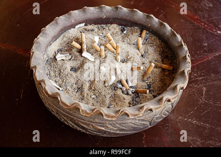 large ceramic ash tray with sand and cigarette butts on a wooden table Stock Photo