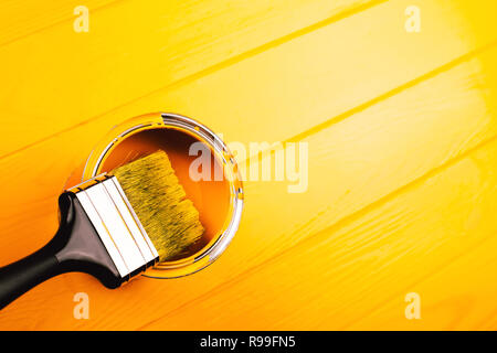 Brush with black handle inside open can of yellow paint on freshly painted wooden board. Renovation concept. Stock Photo