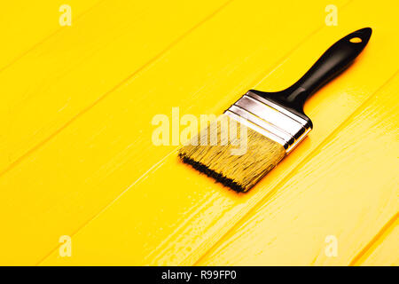 Paintbrush with black handle on yellow freshly painted wooden background. Repairing concept. Vertical photo. Stock Photo