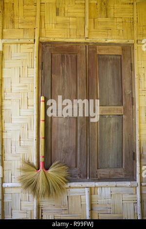 broom hanging on a bamboo bungalow wall with a shuttered window in Laos Stock Photo