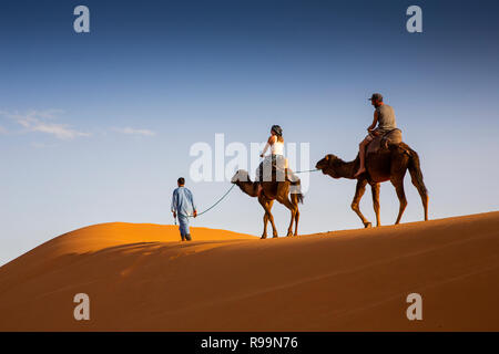 Morocco, Errachidia Province, Erg Chebbi, tourists on camels ride through dunes at sunset Stock Photo