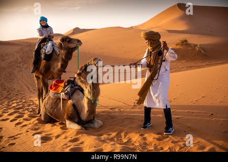 Morocco, Errachidia Province, Erg Chebbi, Berber guide raising camel on ride through dunes Stock Photo