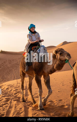 Morocco, Errachidia Province, Erg Chebbi, Berber guide leading tourist on camel on ride through dunes Stock Photo