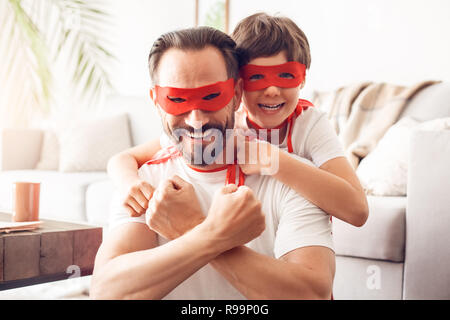 Father and little son wearing superheroe costumes together at home hugging looking camera smiling happy team close-up Stock Photo