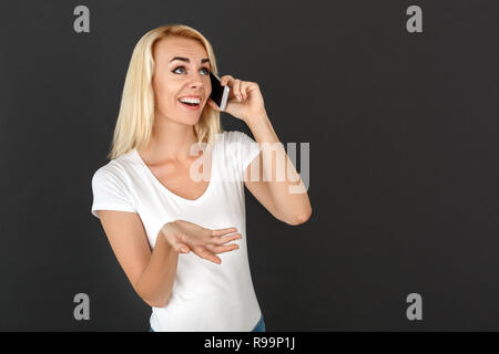 Young woman standing studio isolated on black wall talking on smartphone with friend smiling cheerful Stock Photo
