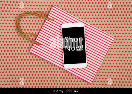 Sale concept - shopping bag and white smartphone with inscription "Shop Now!" on kraft paper background in red polka dots Stock Photo
