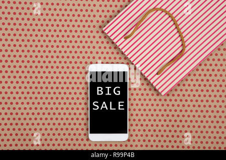 Sale concept - shopping bag and white smartphone with inscription "BIG SALE" on kraft paper background in red polka dots Stock Photo
