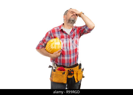 Builder with migraine holding yellow helmet in hand and touching head isolated on white background Stock Photo