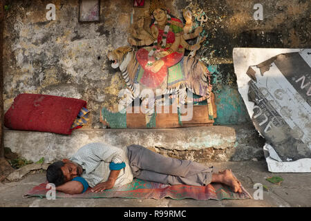 A man sleeps under a cut-out picture of Hindu goddess Durga, depicted riding a tiger, at holy site Banganga Tank, Mumbai, India Stock Photo