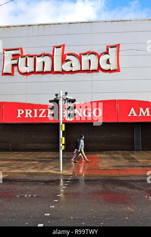 Two people walking along the Promenade in front of a closed Funland amusement arcade on a wet day in winter in Blackpool Stock Photo