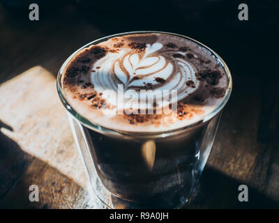 A glass of hot chocolate with leaf latte art on top on wooden table with beautiful light and shadow style. Stock Photo