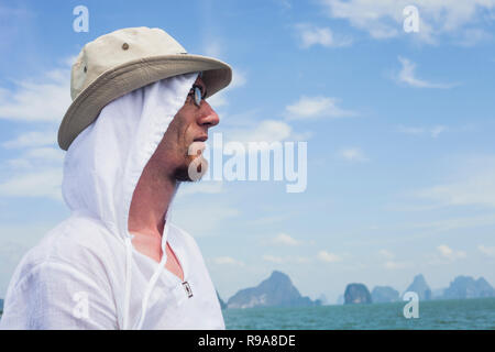 Young man on blue sea and islands silhouettes background, summer tropical vacations. Man wearing white shirt resting near sea Stock Photo