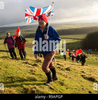 Lockerbie, Scotland, UK. 22nd December, 2018. The climb up Burnswark. A Walk for Peace up Burnswark near Lockerbie in memory of those who died in the Lockerbie Disaster. The walk follows the age-old tradition in Scotland of taking to the hills to find peace and contemplate the future. The walk up Burnswark with the flags of the 21 nations that the victims from the Pan Am flight 103 came from was organises by representatives from Allanton World Peace Sanctuary and local artists Credit: Allan Devlin/Alamy Live News Stock Photo