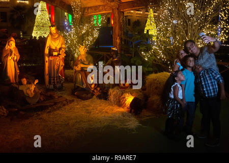 Santo Domingo, Dominican Republic. 21st Dec, 2018. A family photographs a selfie in front of a crib with life-size figures in the main garden of the National Palace. At Christmas the decorated and illuminated government palace opens its doors to visitors. Credit: Pedro Bazil/dpa/Alamy Live News Stock Photo