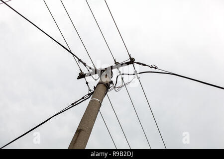 Small concrete pillar with power lines, overcast sky in background. Stock Photo