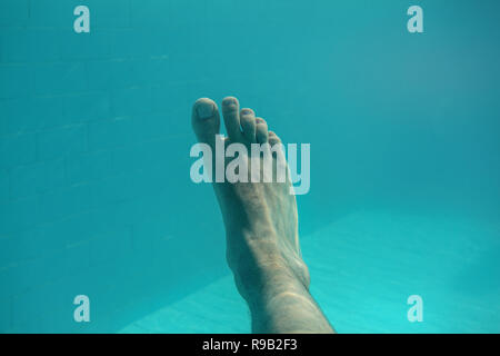 Underwater photo - man's single foot with light blue swimming pool tiles in background. Stock Photo