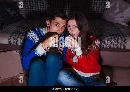 Young couple watching horror movie eating popcorn at home at night Stock Photo