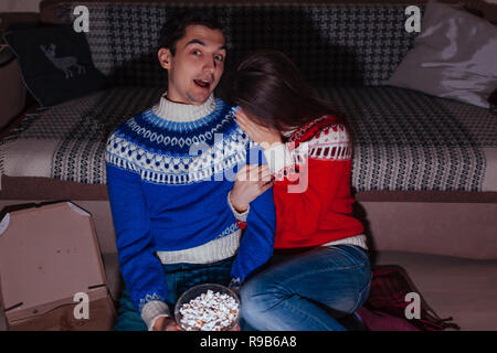 Young couple watching horror movie eating popcorn at home at night Stock Photo