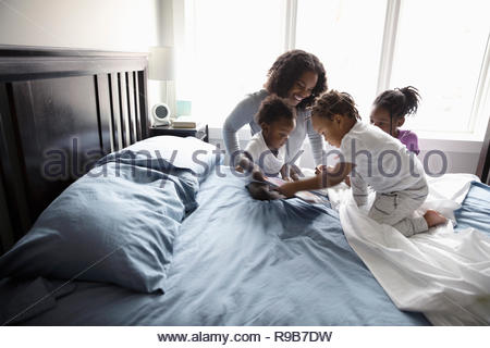 Mother and children with digital tablet on bed
