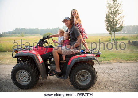Portrait father and young children riding quadbike on farm