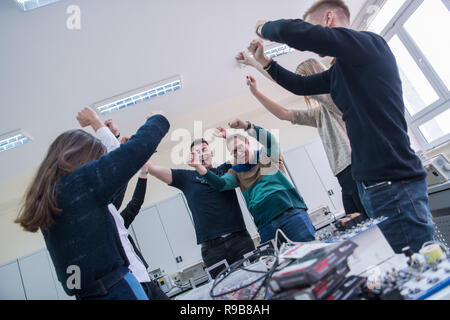 Group of young students in electronics classroom celebrating successfully finished project with holding their hands together, education and technology Stock Photo