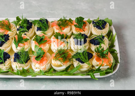 Stuffed eggs with salmon and caviar decorated by parsley, dill and arugula. Party food Stock Photo