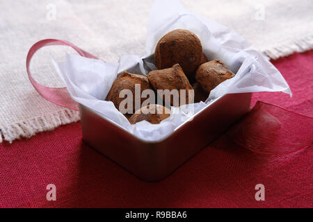 Chocolate truffles in metal box on red an beige background with ribbon Stock Photo