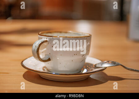 Side view of Empty ceramic cup on wooden table with silwer spoon near on sourcer Stock Photo