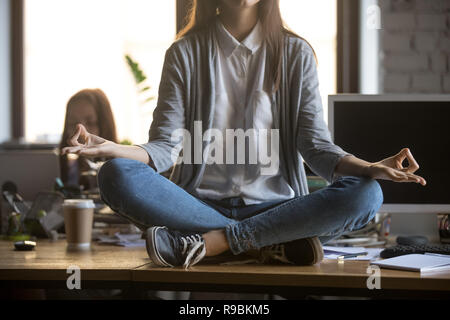 Woman sitting on desk in lotus position doing yoga exercise Stock Photo