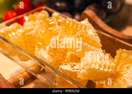 Closeup of fresh honeycombs cut into cubes in a transparent square glass bowl on the table. The concept of a delicious breakfast at the hotel on the b Stock Photo