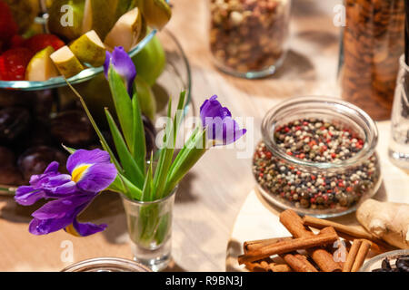 Closeup snacks, purple irises, fresh and dried fruits, red, white and black pepper mix in glass bowl, cinnamon sticks, nuts. Concept degustation premi Stock Photo