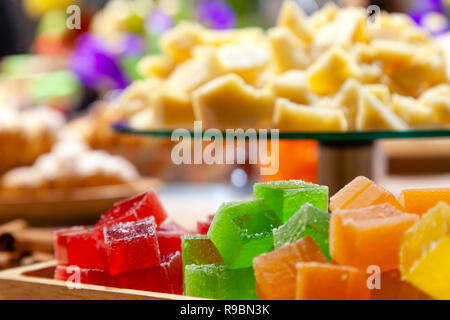 Closeup of stacks of small cubes of green, red, yellow, orange marmalade, glass round plate with hard parmesan cheese on rectangular wooden plate on a Stock Photo