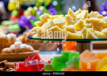 Closeup of stacks of small cubes of green, red, yellow, orange marmalade, glass round plate with hard parmesan cheese and croissants on rectangular wo Stock Photo