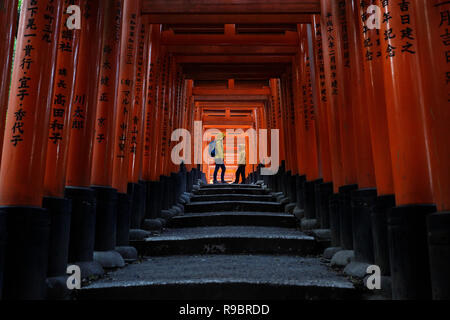 Mother and son in yellow jackets in the beautiful tunnel of torii doors in the Fushimi Inari shrine of Kyoto, Japan Stock Photo