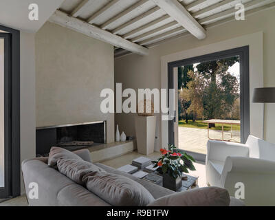 interiors shots of a modern living room with sofas and armchair in front of a fireplace overlooking on the garden Stock Photo