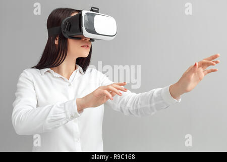 Young woman wearing virtual reality headset studio standing isolated on gray wall playing game concentrated Stock Photo
