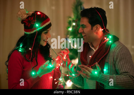 young couple wrapped fairy light at Christmas Celebrations Stock Photo