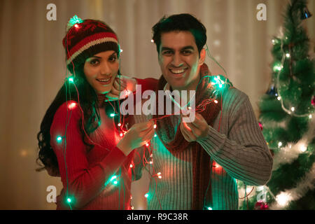 young couple wrapped fairy light at Christmas Celebrations Stock Photo