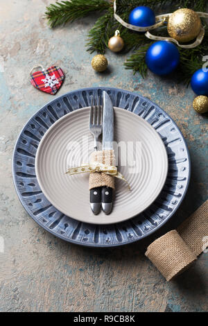 Christmas table setting on decor background. Blue and gray plate, cutlery, gift box and decorations. Top view. Stock Photo