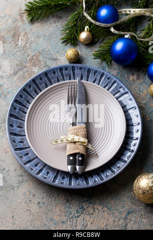 Christmas table setting on decor background. Blue and gray plate, cutlery, gift box and decorations. Top view. Stock Photo