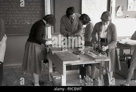 1950s, historical picture of three schoolgirls at a workbench doing a woodwork class, with a male teacher examing a girl's work, England, UK Stock Photo