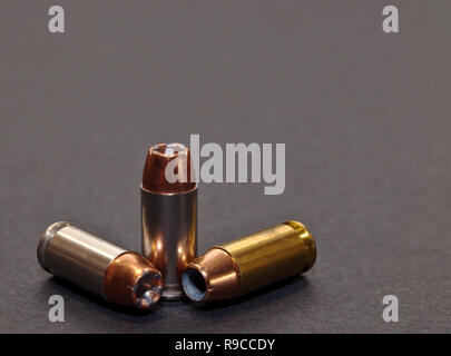 Three 40 caliber hollow point bullets on a gray background. Two with silver cases and one with brass with added room for text Stock Photo