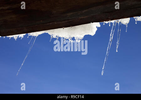 Wooden roof with snow cornice and icicles at sun winter day. Bottom view. Selective focus. Stock Photo