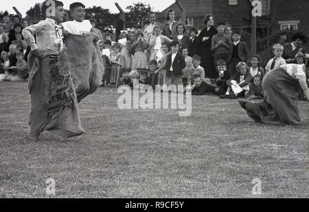 1950s, historical, young schoolboys competing outside on a grass field in a sack race, at a primary school sports day, cheered on by watching parents and other school children, England, UK. Stock Photo