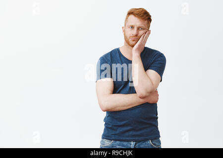 Father left alone with kids, feeling bored, wanting come and drink beer with guys. Upset and tired good-looking masculine male with red hair and bristle, leaning on palm from boredom and indifference Stock Photo