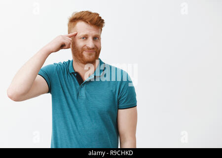 Redhead displeased guy discussing weird friend who got insane recently, making stupid decisions. Portrait of mature european man rolling finger on temple and mocking someone who make fool of himself Stock Photo