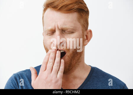 Headshot of tired attractive male entrepreneur with red hair and beard, yawning with closed eyes, covering opened mouth with palm, feeling tired, sleepy after taking nap or waking up early in morning Stock Photo
