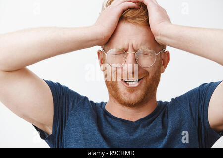 Man crying thinking why he is one who got in trouble. Whining displeased cute redhead in glasses holding hands on head, closing eyes and frowning, suffering from bad feelings and negative emotions Stock Photo